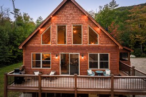 A wooden cabin with a deck, large windows, and a staircase leading to the entrance.