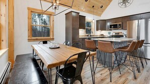 A modern kitchen with wooden cabinets, a stainless steel refrigerator, and a dining area with a wooden table and chairs.