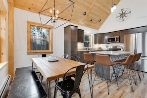 A modern kitchen with wooden cabinets, a stainless steel refrigerator, and a dining area with a wooden table and chairs. - Paradise Valley Lodge (Bethel)