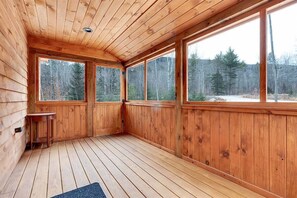 A wooden cabin with large windows, a wooden deck, and a small table. - Paradise Valley Lodge | Hot Tub & Game Room (Bethel)