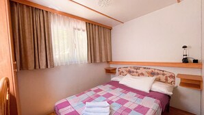 Ein Schlafzimmer mit einem Bett, einem fenster mit Vorhängen, einem Nachttisch mit Lampe und einem Kopfteil mit Musterdesign.