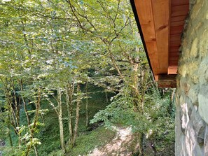 Ein Steinhaus mit Holzdach, umgeben von einem bewaldeten Gebiet mit einem Feldweg.