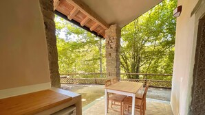 Ein Balkon mit Tisch und Stühlen, einer Steinsäule und Blick auf Bäume.