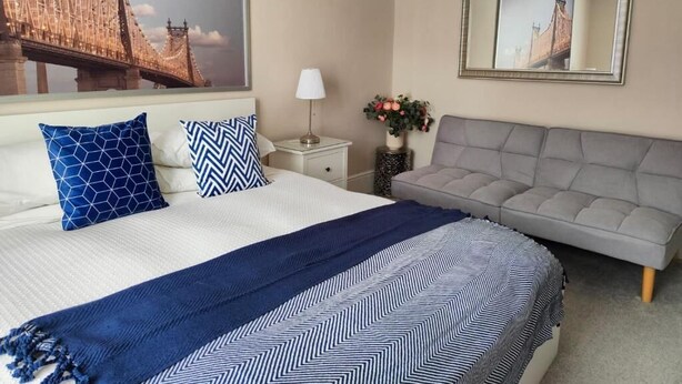 Hotelkamer met een bed, een grijze bank, een spiegel, een nachtkastje met een lamp en een wandairconditioner.