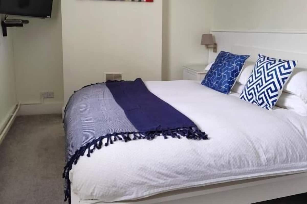 Un dormitorio con cama, televisor de pantalla plana montado en la pared y una pintura de paisaje urbano sobre la cama.