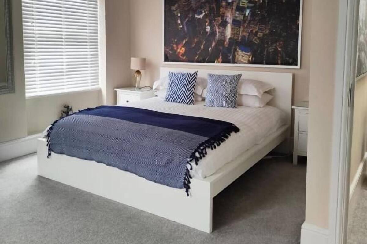 Un dormitorio con una cama grande, una mesita de noche, una lámpara y un cuadro de un paisaje urbano en la pared.