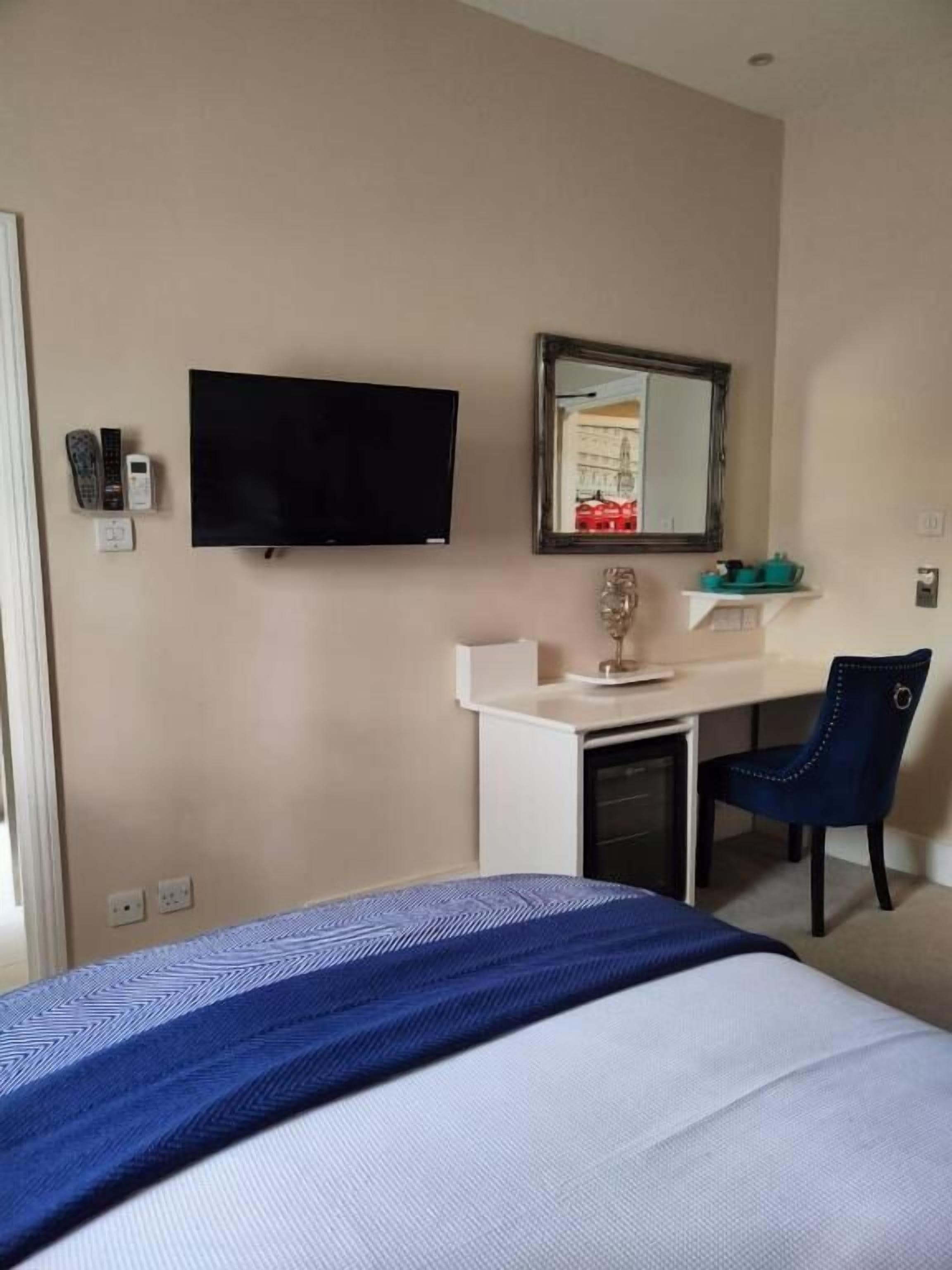 A hotel room with a bed, a desk, a chair, a television, and a mirror.
