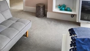 Een moderne woonkamer met een grijze bank, een salontafel, een televisie en een wandklok.