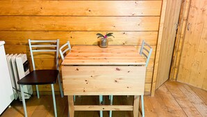 A wooden-paneled room with a wooden table and four chairs, a radiator, and a small potted plant.