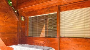 Ein Holzblockbau-Innenraum mit Esstisch, Stühlen und einem Fenster mit Jalousien.