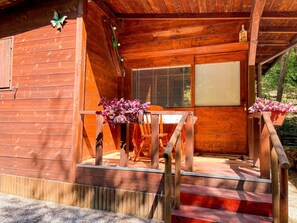 A wooden cabin with a porch, a window with blinds, and a number plaque. - Caravan "Le Sorgenti - Chalet 12" with Mountain View & Private Garden (Palazzuolo Sul Senio)