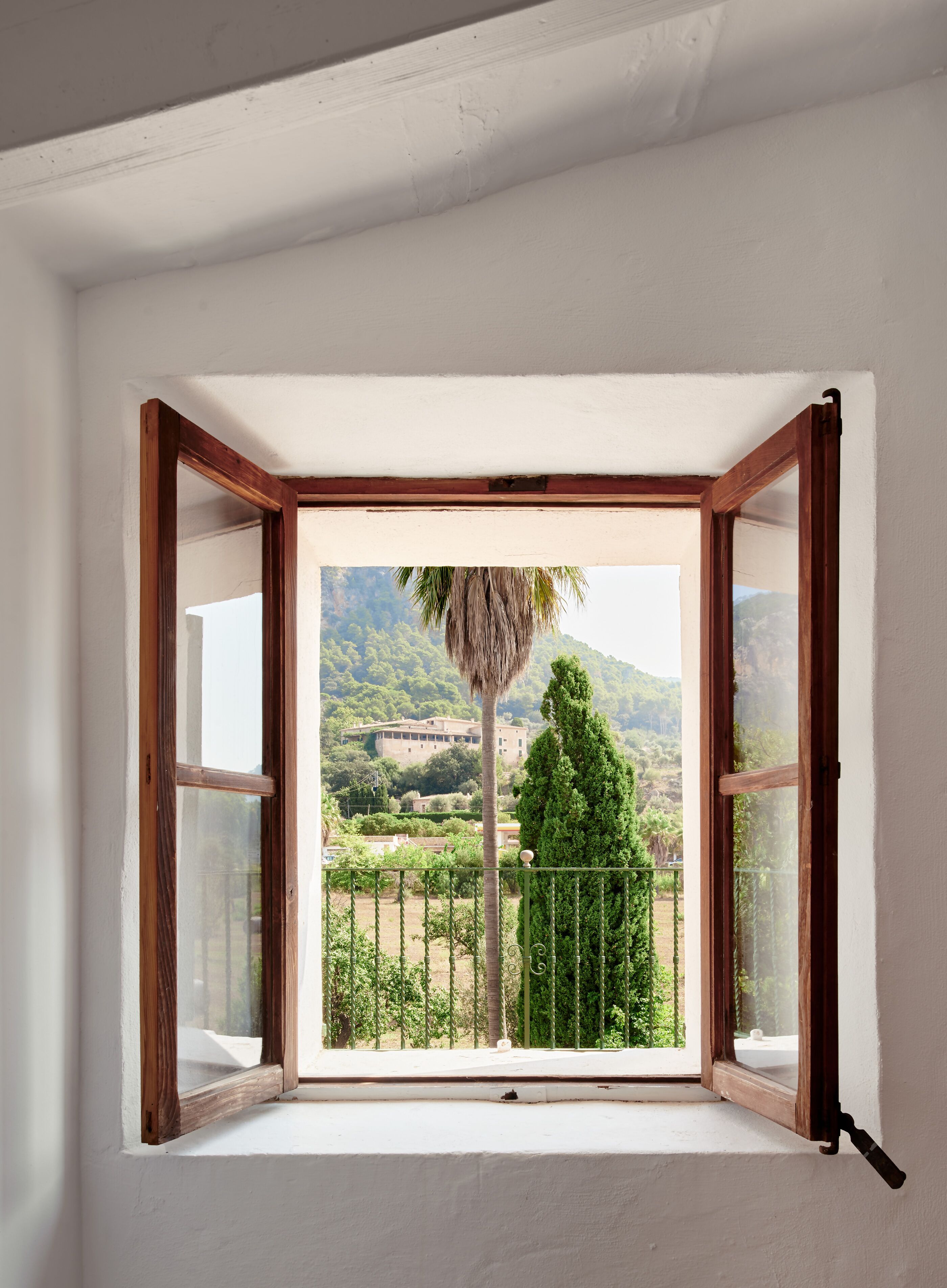 Ein offenes Fenster mit Blick auf eine Berglandschaft und ein Gebäude in der Ferne.