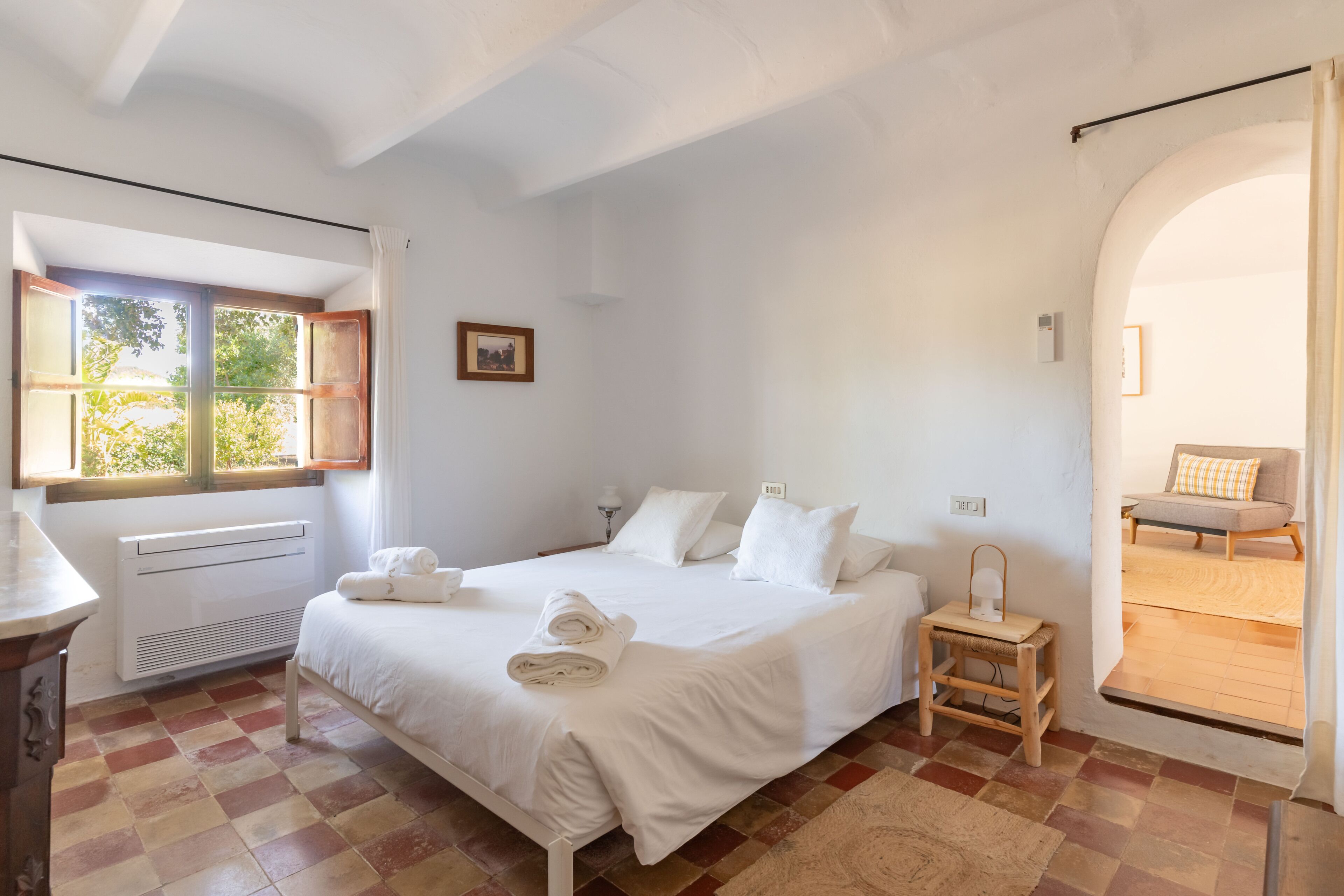 A bedroom with a bed, a radiator, a window, and a door leading to another room.