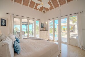 A bedroom with a large bed, a ceiling fan, and a view of an outdoor pool area.