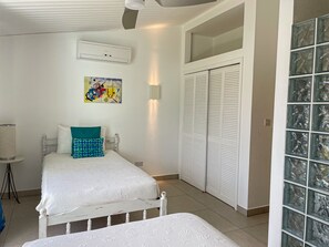 A bedroom with a bed, a bedside table, a wall-mounted air conditioner, a painting, a closet with louvered doors, and a glass door. - Beautiful Waterfront Villa (Jolly Harbour)