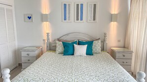 Une chambre à coucher bien rangée, avec un lit, deux tables de chevet, une petite table et un luminaire fixé au mur.