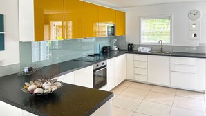 Une cuisine moderne avec des meubles blancs et jaunes, un plan de travail noir et une fenêtre équipée de stores.