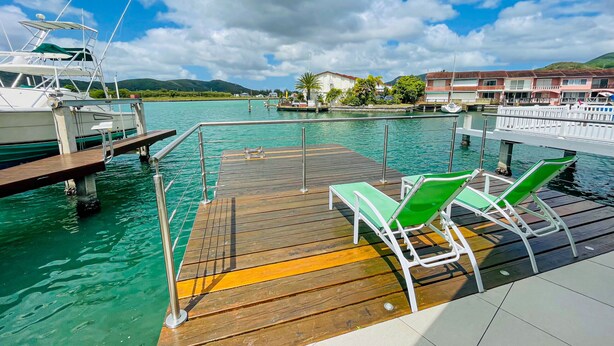 Une jetée en bois avec des fauteuils de jardin verts et un bateau amarré à proximité.