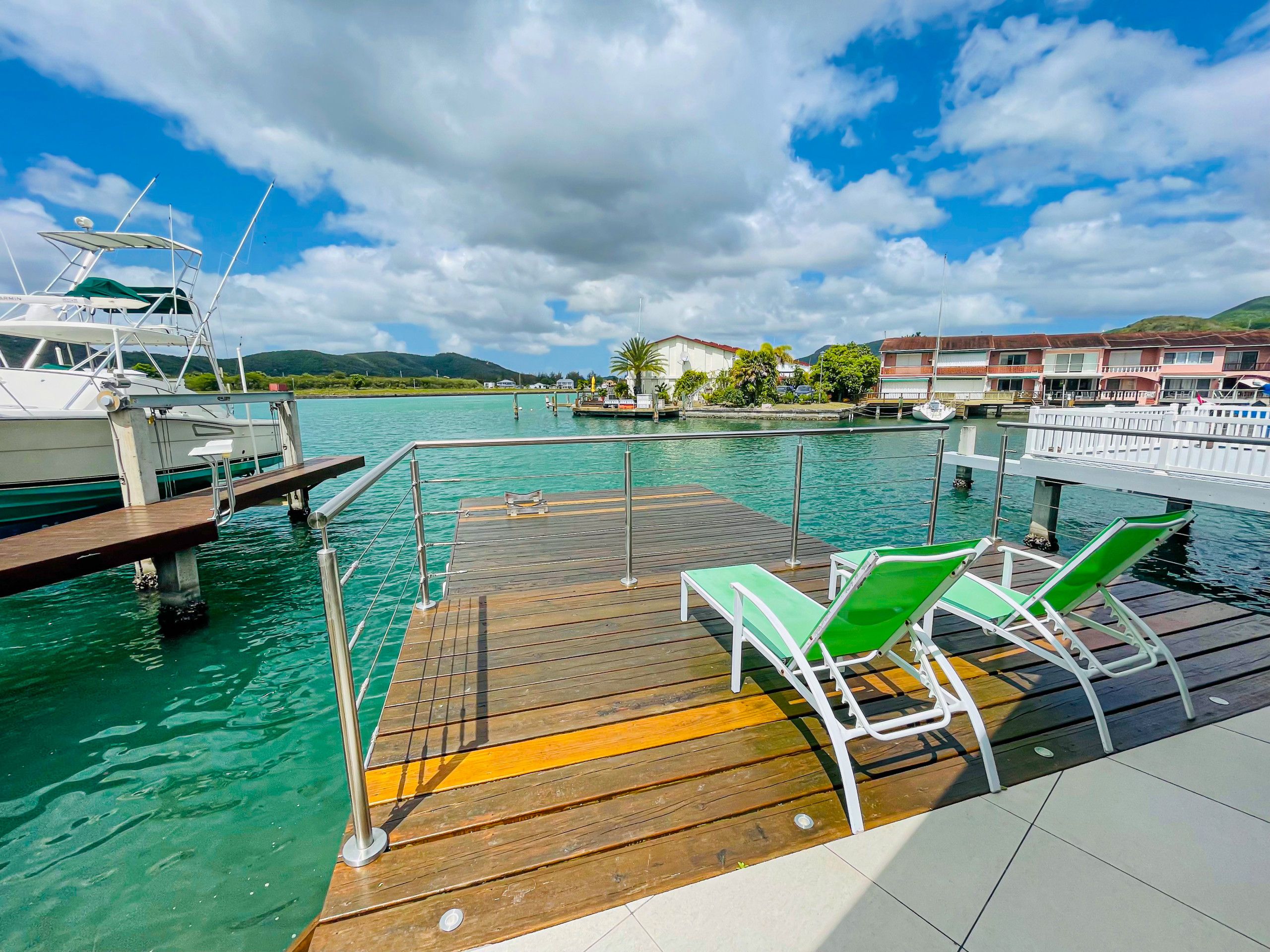 A wooden dock with green lounge chairs and a boat docked nearby.