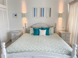 A neatly arranged bedroom with a bed, two bedside tables, a nightstand, and a wall-mounted light fixture.