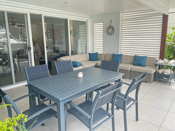 An outdoor patio area with a dining table and chairs, a sofa with cushions, and a decorative wreath on the wall.