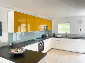A modern kitchen with white and yellow cabinets, a black countertop, and a window with blinds.