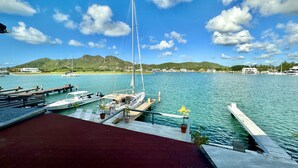 A marina with docked boats, a sailboat, and a view of a mountainous landscape under a partly cloudy sky. - Modern Waterfront Villa (Jolly Harbour)