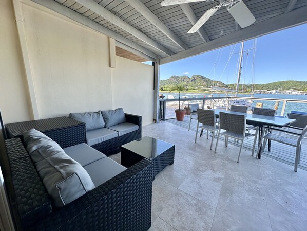 A covered outdoor seating area with a sofa and chairs, a table, and a view of the marina. - Modern Waterfront Villa (Jolly Harbour)