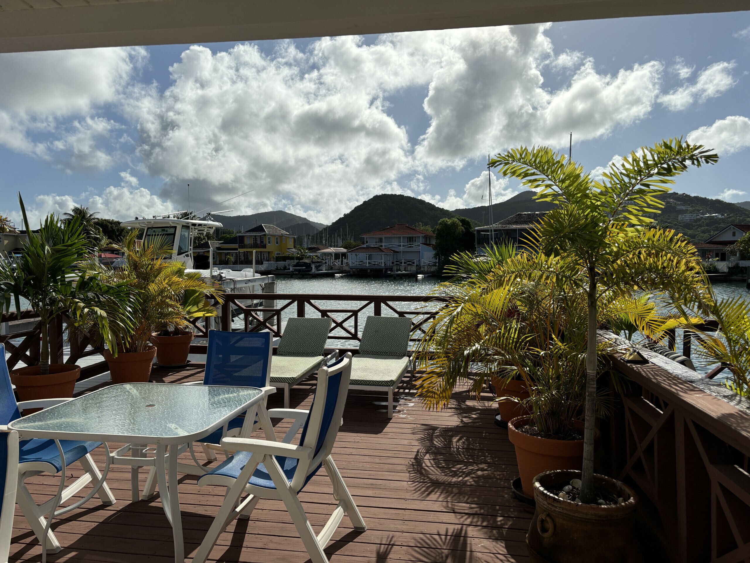 A wooden deck with a glass table and chairs, overlooking a marina with boats and houses.
