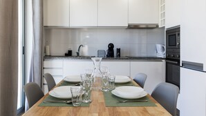 A modern kitchen with white cabinets, a wooden dining table set with plates and glasses, and a coffee maker.
