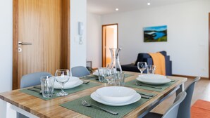 A dining table set with plates, glasses, and cutlery, with a wooden floor and a painting on the wall.