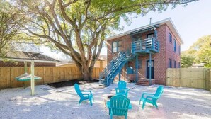 A two-story brick building with a blue staircase, outdoor seating area with turquoise chairs, and a large tree providing shade. - Downing Street Retreat B wifi, firepit, hammock (Jacksonville)