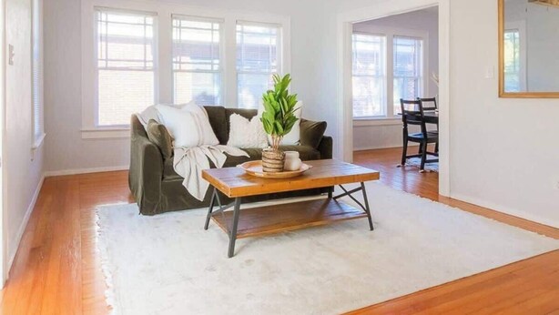 A spacious living room with hardwood flooring, a white rug, a sofa, a coffee table, and a ceiling fan. - Downing Street Retreat B wifi, firepit, hammock (Jacksonville)