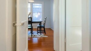 A hallway with wooden flooring, a dining area with a table and chairs, and a window with blinds. - Downing Street Retreat B wifi, firepit, hammock (Jacksonville)