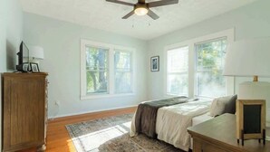 A bedroom with a bed, a desk, a chair, a ceiling fan, and large windows. - Downing Street Retreat B wifi, firepit, hammock (Jacksonville)