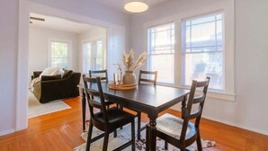 A dining area with a wooden table, four chairs, a hanging light fixture, and large windows. - Downing Street Retreat B wifi, firepit, hammock (Jacksonville)