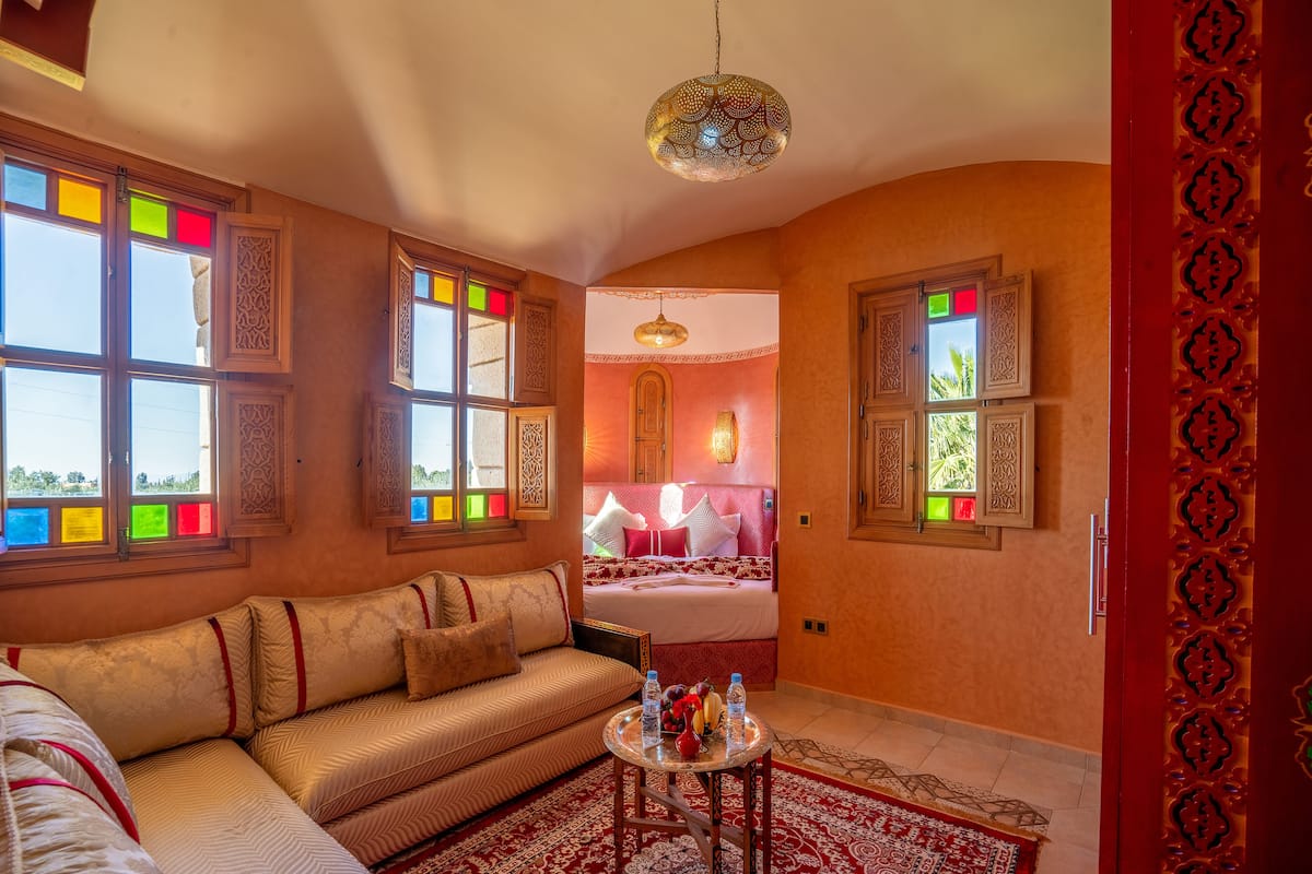 A room with a sofa, a small round table with bottles, and a patterned rug.