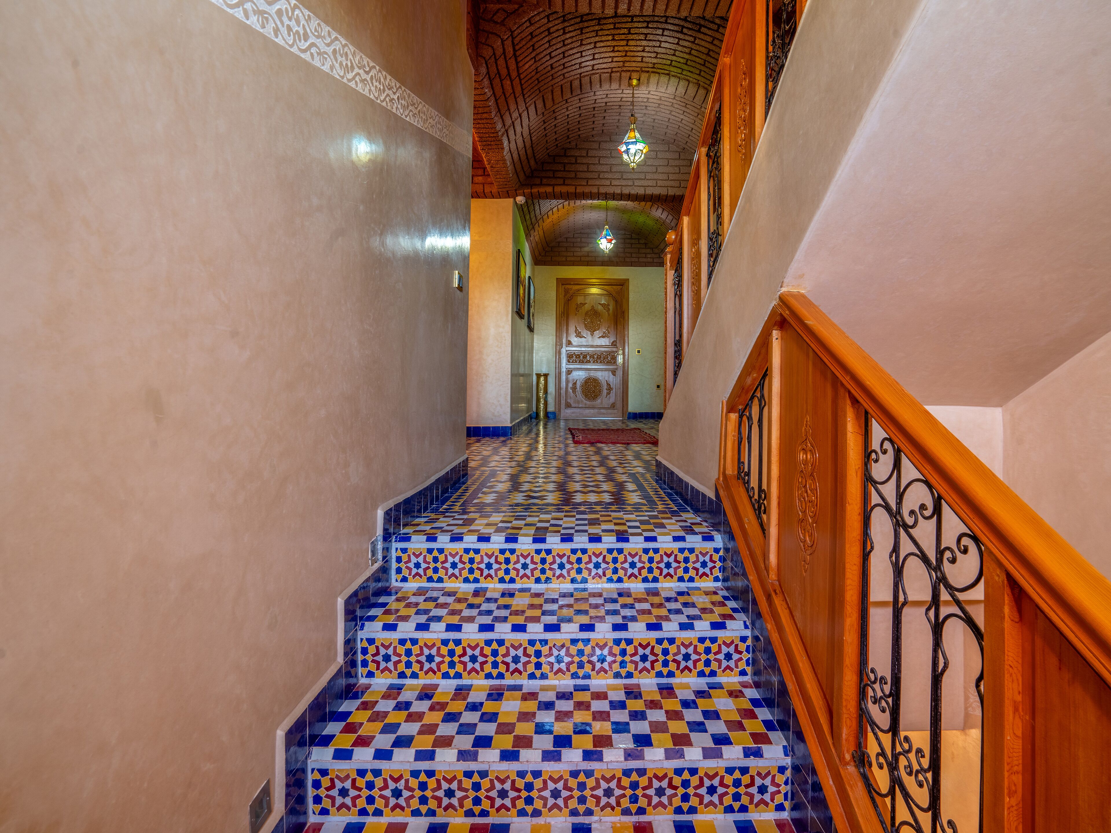 A staircase with a checkered tile pattern leading to a room with a patterned ceiling and a wooden railing.