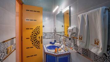 A bathroom with a yellow door, a sink with a blue and gold design, a towel rack with a white towel, and a hairdryer.