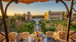 A dining area with a table set for breakfast, overlooking a pool and a castle-like building. - Atlas Castle Marrakech (Ghmate)