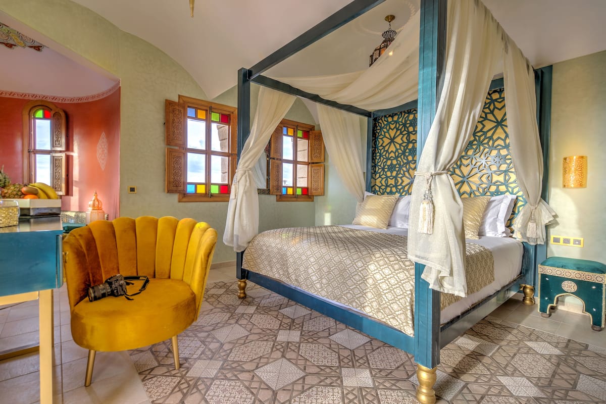 A four-poster bed with a canopy, a yellow chair, and a small side table with a lamp.
