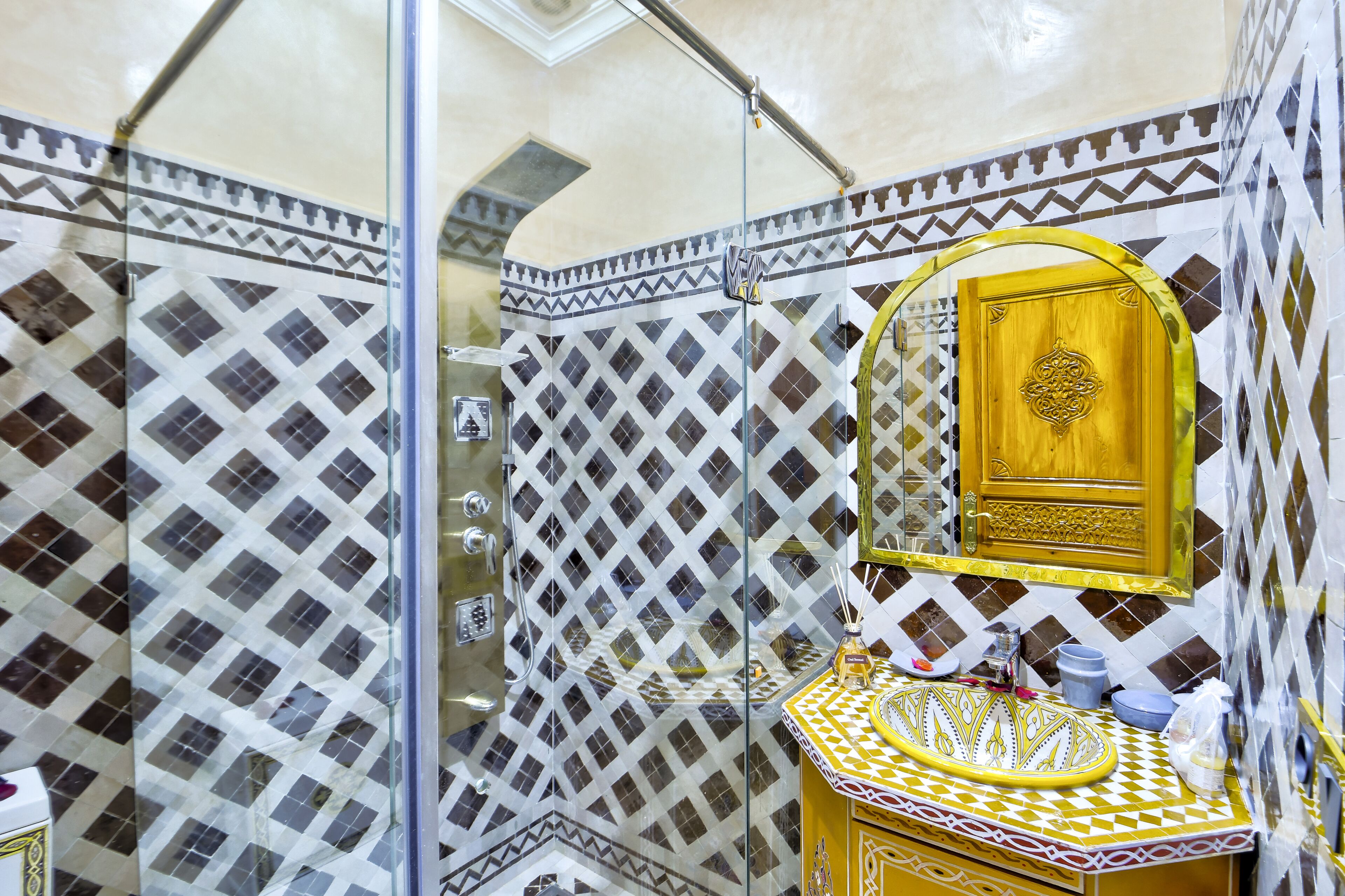 A bathroom with patterned tiles, a glass shower enclosure, a wooden cabinet with a mirror, and a sink with a patterned countertop.