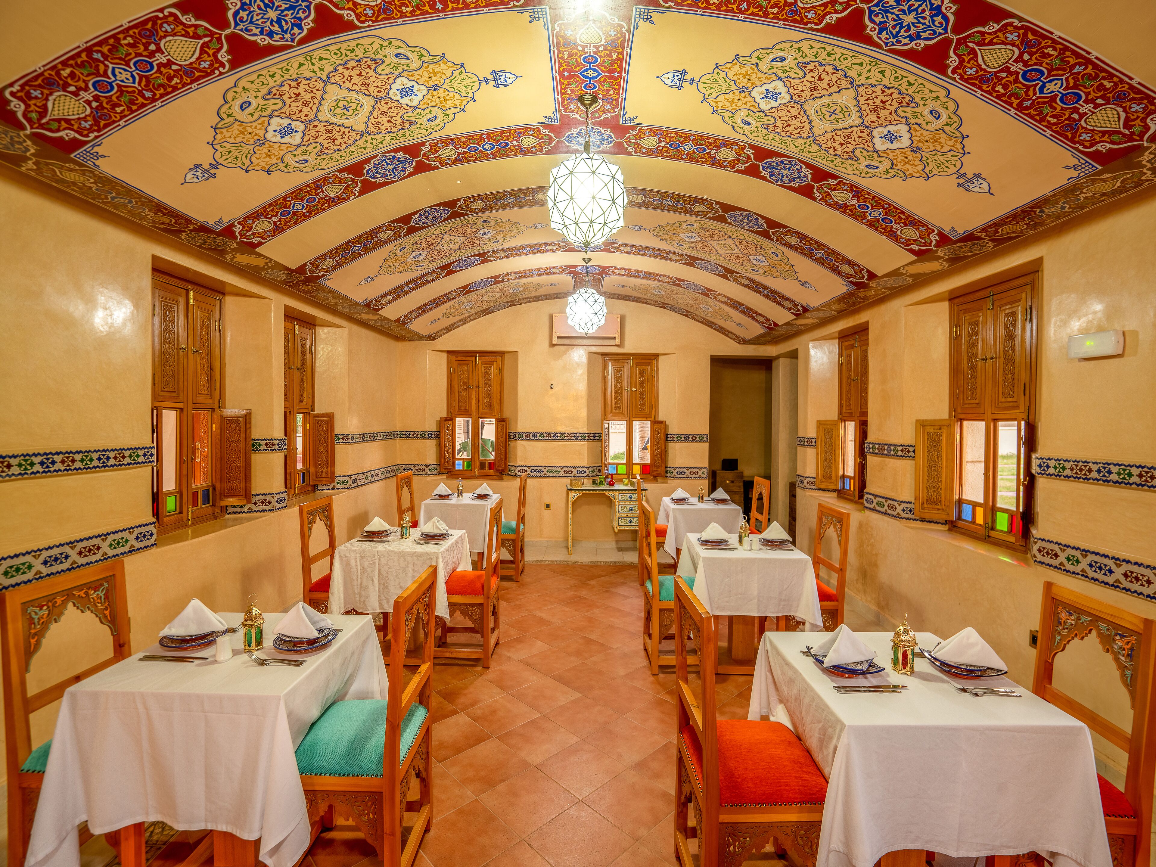 A dining area with tables set for two, wooden chairs, and a chandelier.