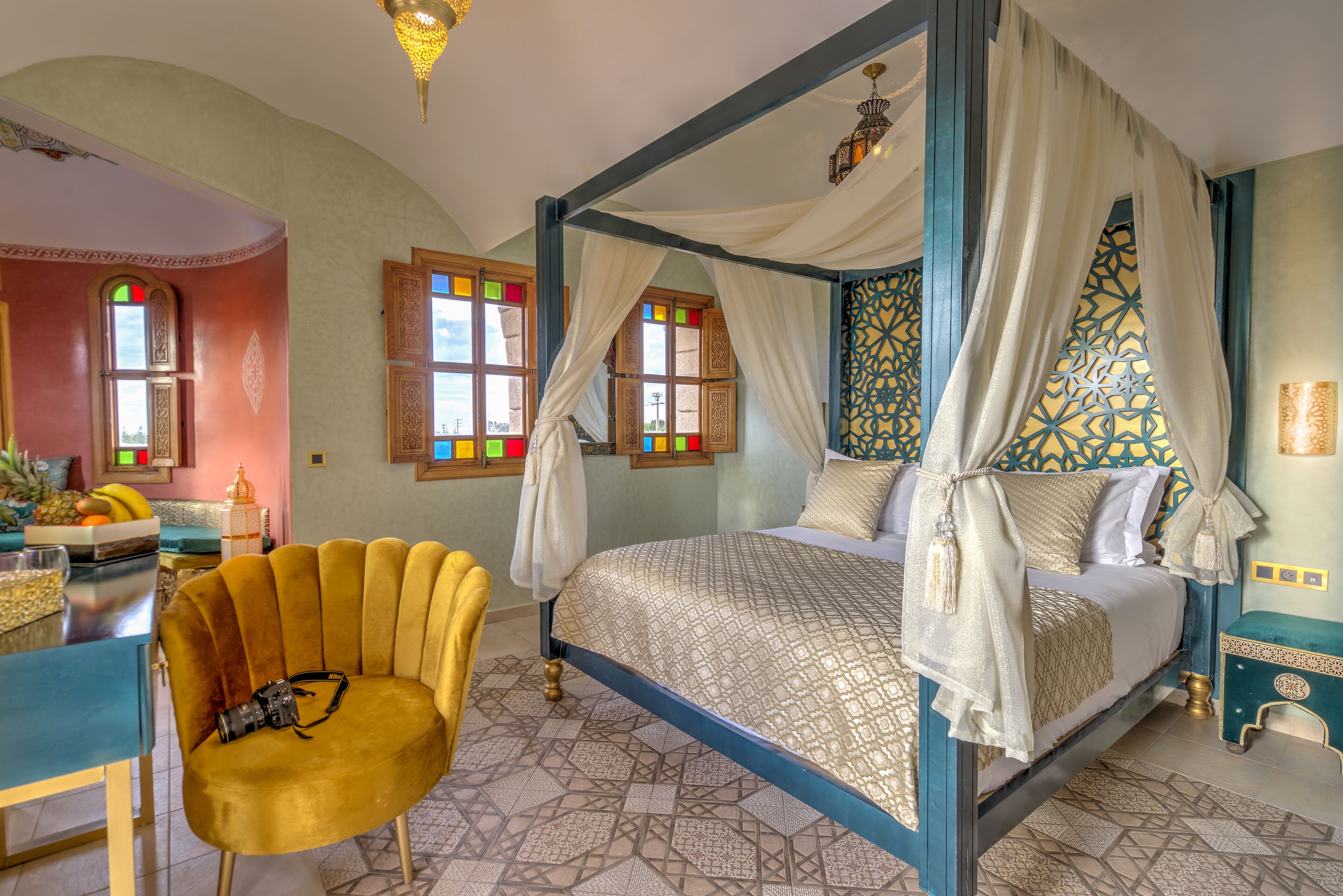 A four-poster bed with a canopy, a chair with a camera, and a breakfast bar with fruit.