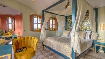 A four-poster bed with a canopy, a chair with a camera, and a breakfast bar with fruit.