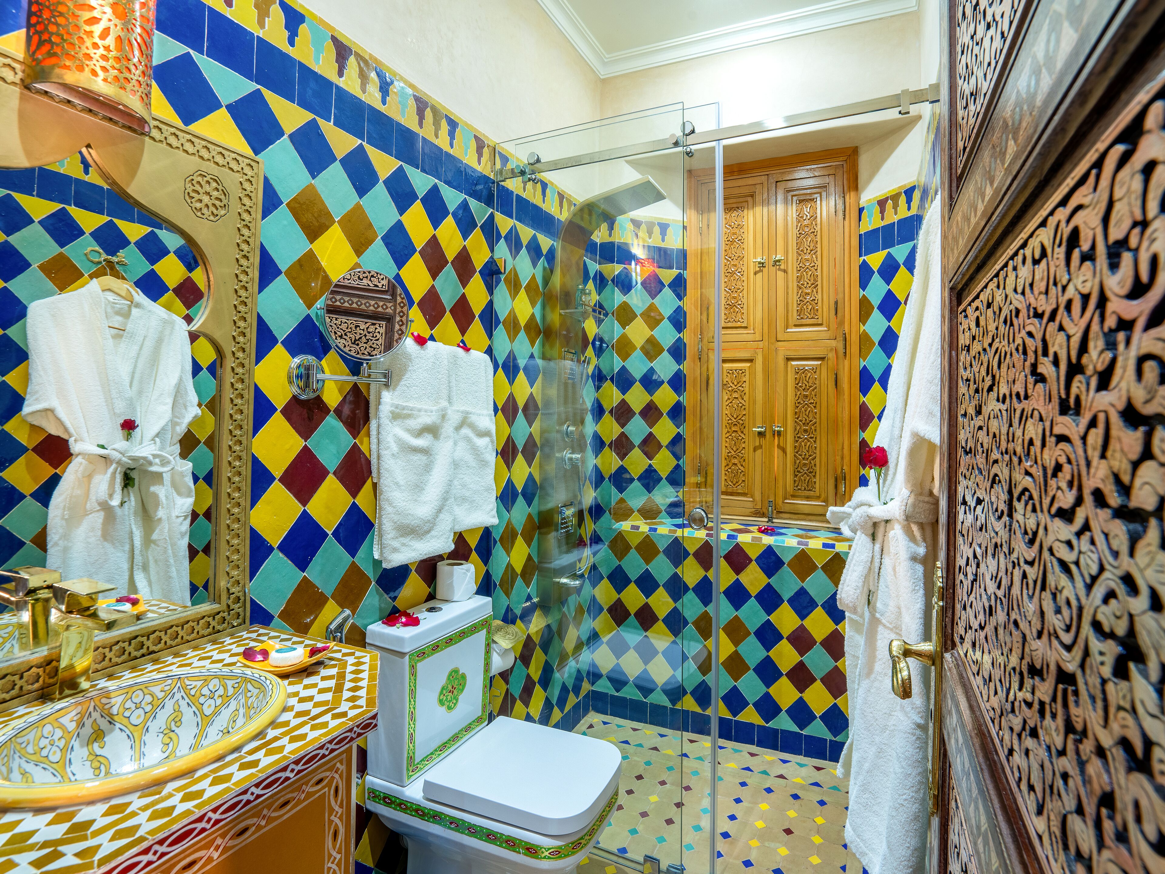 Ein Badezimmer mit farbenfroher, diamantmuster-gefliester Wand, einer weißen Toilette, einem Waschbecken mit gemustertem Becken und einer Duschkabine aus Glas.