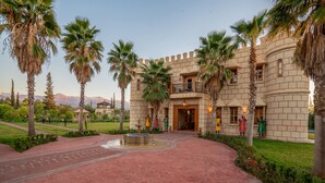 A courtyard with a fountain, palm trees, and a building with a turreted entrance. - Atlas Castle Marrakech (Ghmate)