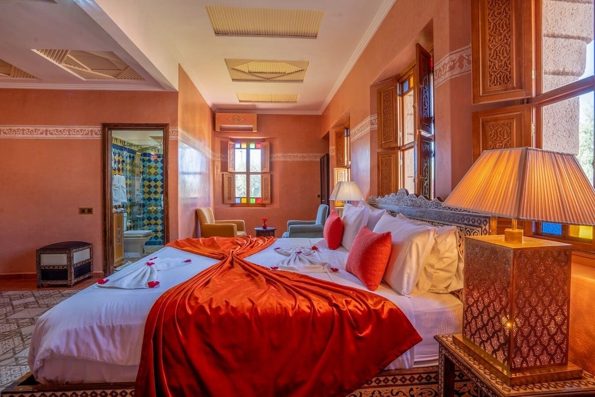 A hotel room with a large bed, a sitting area with a chair, a small table, and a decorative lamp.