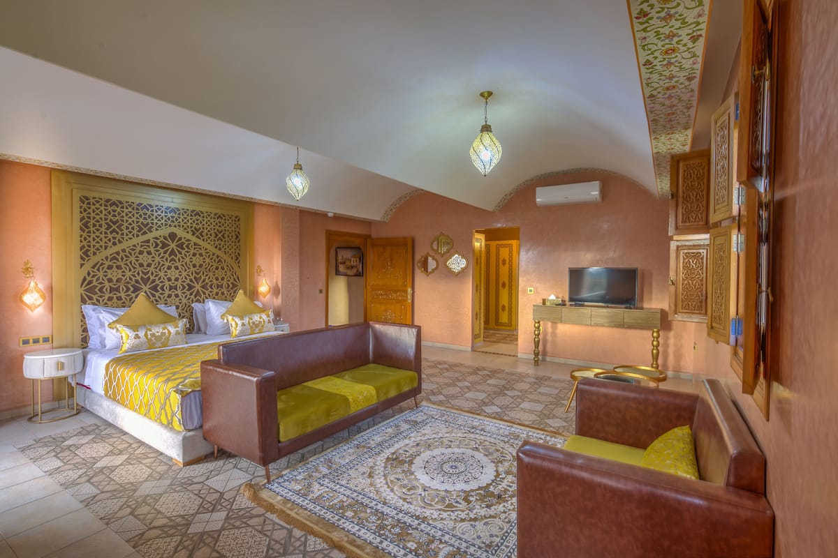 A hotel room with a bed, two sofas, a TV, and decorative wall panels.