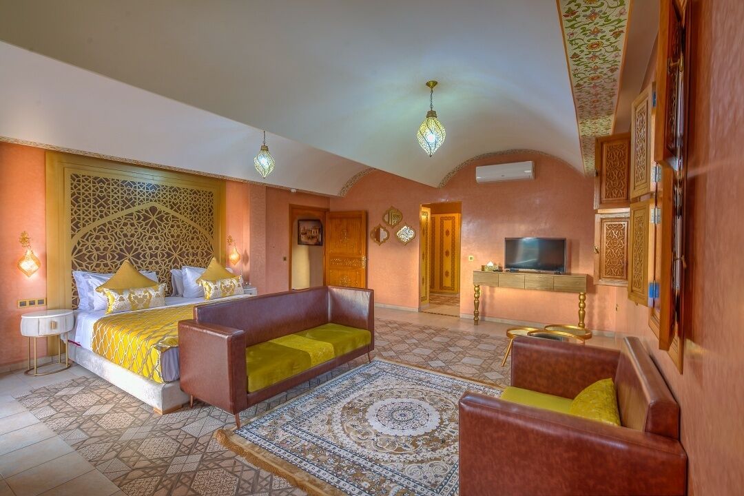 A hotel room with a bed, two sofas, a TV, and a decorative ceiling.